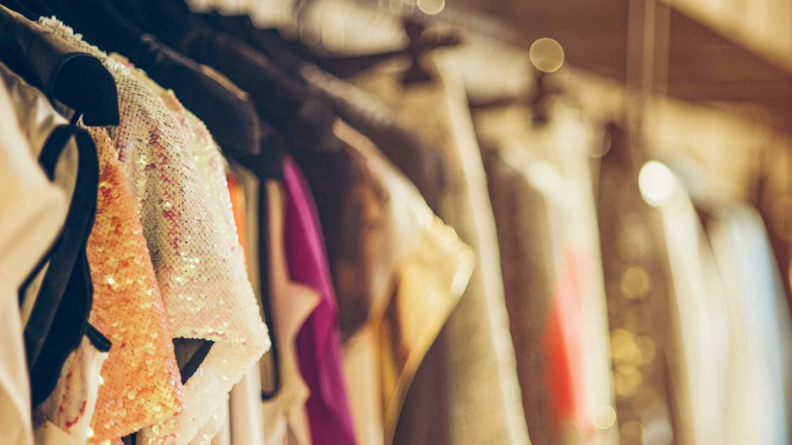 A row of numerous women's dresses hanging in a closet. The dresses come in several colors, patterns, and styles.