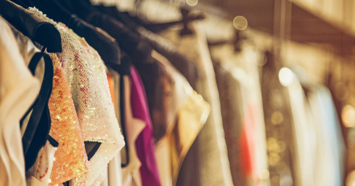 A row of numerous women's dresses hanging in a closet. The dresses come in several colors, patterns, and styles.