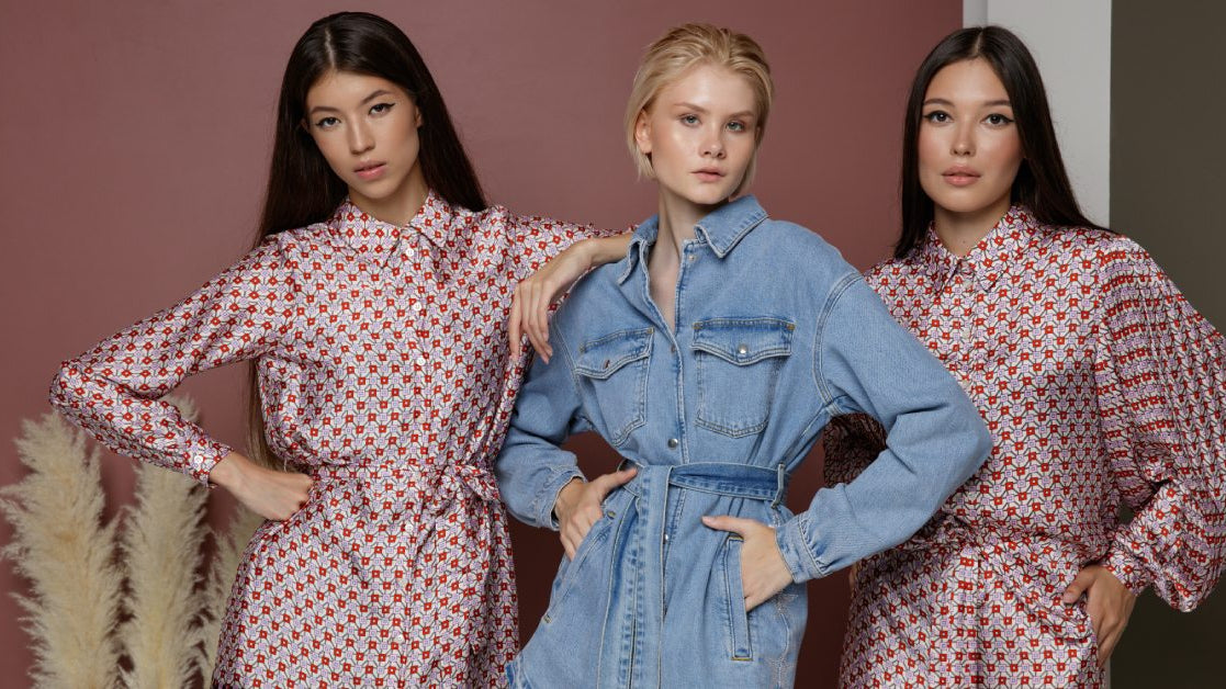 Three fashion models--one wearing a dress, one wearing a romper, and one wearing a jumpsuit--all pose for the camera.
