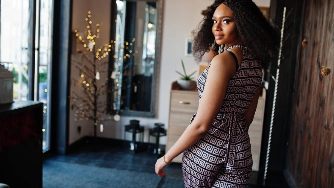 A young woman wearing a black patterned jumpsuit and looking over her shoulder as she walks.