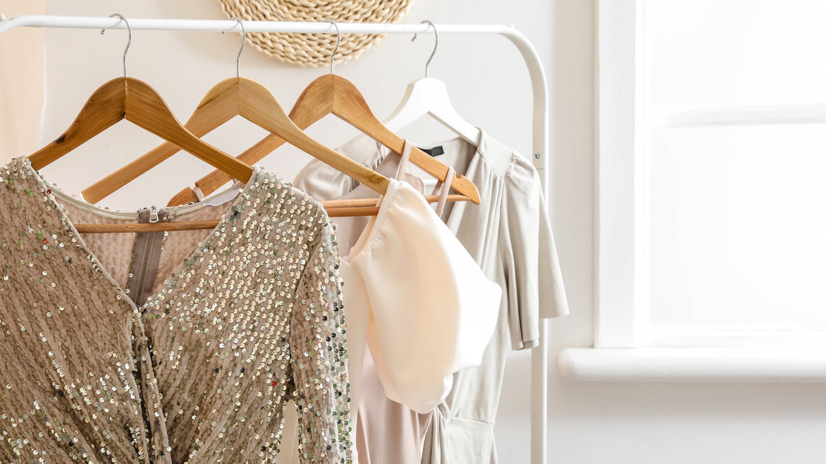 A close-up of a clothing rack holding different garments, including a sequin dress, a pink dress, and a beige dress.