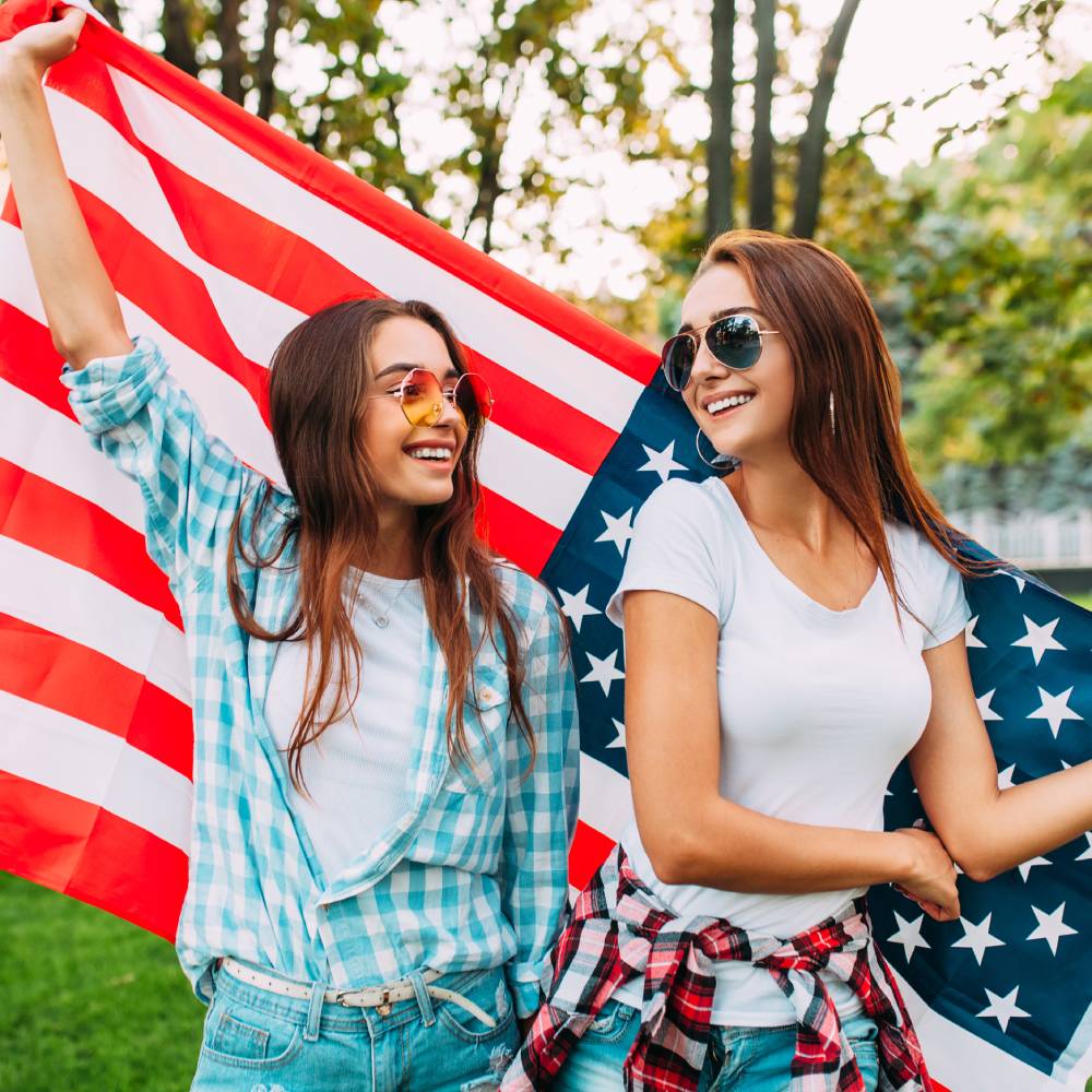 Two girls wearing festive Fourth of July clothing colors and holding the United States flag behind them