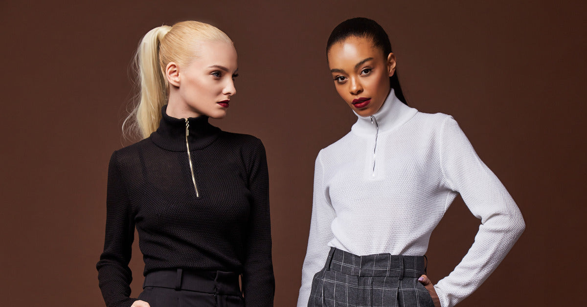 Two stylish women wearing zip-up sweater sweatshirts with tailored pants. They strike cool poses against a marron backdrop.