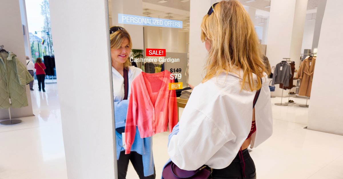 A woman standing in front of an interactive mirror in a clothing store. A pink cashmere cardigan appears in the mirror.