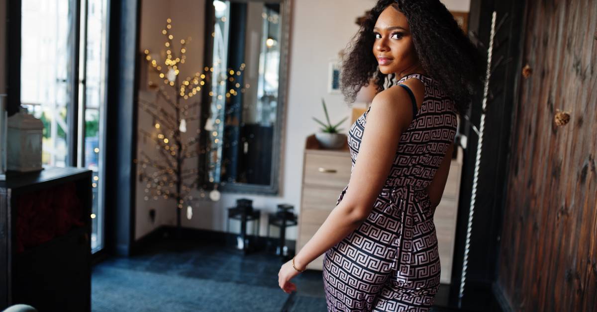 A young woman wearing a black patterned jumpsuit and looking over her shoulder as she walks.