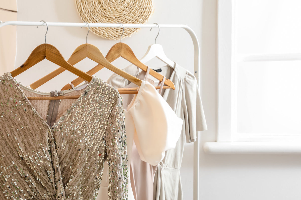 A close-up of a clothing rack holding different garments, including a sequin dress, a pink dress, and a beige dress.